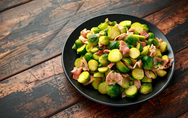 Roast Brussel Sprouts with Bacon on black plate. wooden table