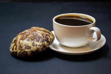 a white cup with coffee on a black background next to a gingerbread