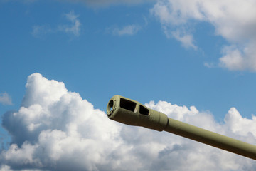 Naklejka na ściany i meble Close-up of a heavy tank or howitzer gun with a muzzle brake against a blue sky with clouds. 