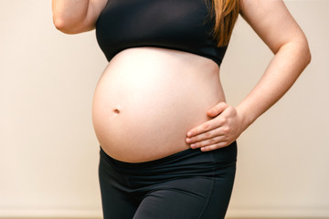 Image of the stomach of pregnant woman at last ninth month in the top and leggings, arms hugging...