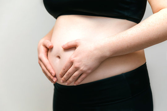 Image of the stomach of pregnant woman in the top and leggings, arms hugging her stomach. Pleasant expectation baby