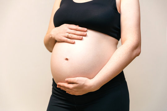 Image of the stomach of pregnant woman at last ninth month in the top and leggings, arms hugging her stomach. Pleasant expectation baby