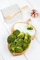Cooked broccoli on a wooden plate. Cabbage served with sauce. Culinary healthy vegetarian food. Top view.