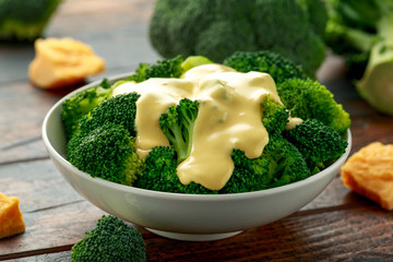 Broccoli with cheese sauce in white bowl on wooden table