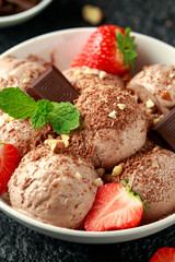Fototapeta na wymiar Chocolate Ice Cream with dark chocolate bars, strawberry and hazelnuts in a white bowl