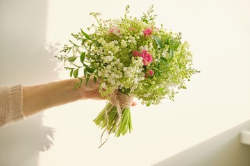Beautiful fresh bouquet of lily of the valley flowers, pink rose, green branches in woman hand