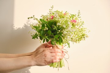 Beautiful fresh bouquet of lily of the valley flowers, pink rose, green branches in woman hand