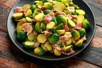 Roast Brussel Sprouts with Bacon on black plate. wooden table