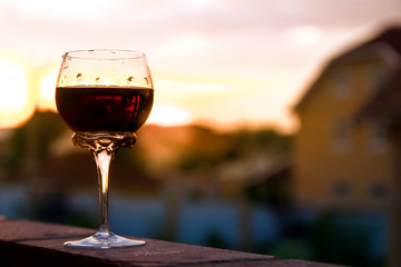 A glass of wine stands on the balcony railing. The view of the sunset and the city. Rest and relaxation after work.