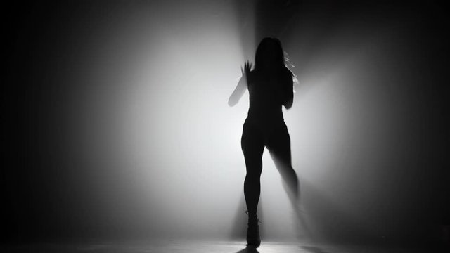 Slim sexy silhouette of woman dancing on smoke dark stage in front of light projector. Concept of arts, flexibility, talented girl. 4k