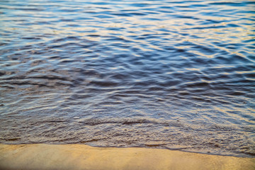 A small wave beats on the shore of the river, lake, sea. Blue shade of water. Close-up of the wave. Calm water. Background.