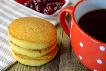Homemade oatmeal cookies, cup of coffee or tea, and jam in saucer on napkin on wooden table. Use to display traditional quick and tasty breakfast or tea party. Selective focus.