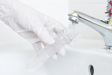 Tap water analysis quality control concept. Hand with a flask and water tap ckose up.