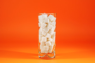 Glass full of sugar cubes on orange background. Diabetes, sugar disease, unhealthy food, diet...