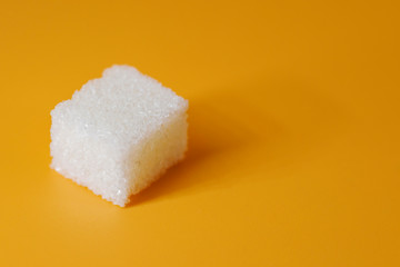 One single piece cube sugar on yellow background. Sugar cube