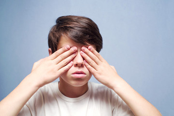 Boy covering eyes with her hands on a blue background 