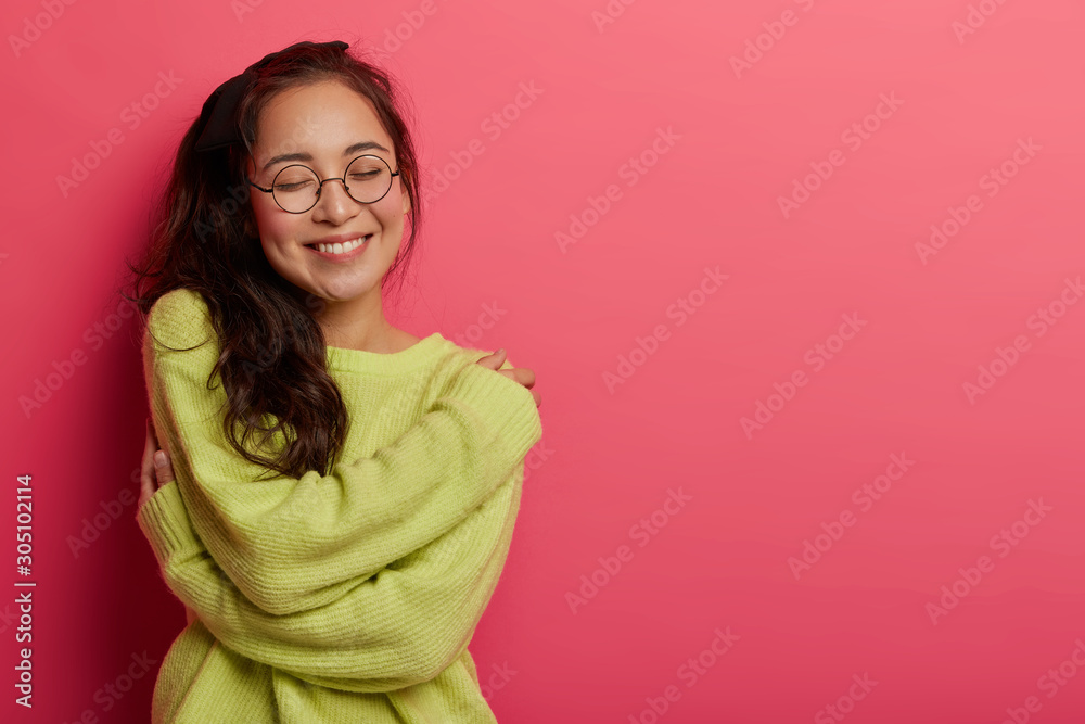 Wall mural photo of charming woman expresses self love and care, enjoys wearing new soft green sweater, embrace