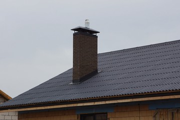 one brick chimney on the brown tiled roof of a private house against the sky