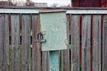 iron green box for electricity on the street by a gray wooden fence