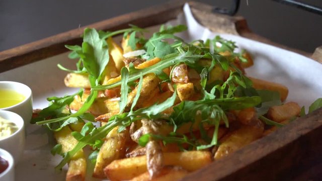 Parmesan cheese falling on french fries made of fresh potatoes with rocket salad in slow motion