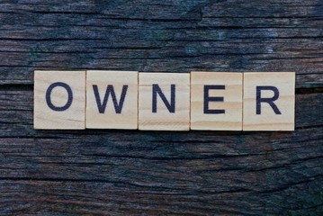 Fototapeta premium word owner made from brown wooden letters lies on a gray wood board