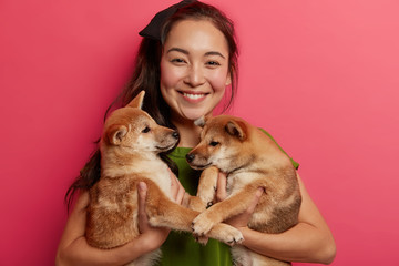 Pets, animals, people concept. Glad Asian woman poses with two small puppies, likes shiba inu dogs, smiles broadly, gets good news from vet, happy to have healthy pets. Time to visit groomer