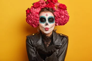 Foto der schönen Frau bläst mwah, hält die Lippen gefaltet, trägt kreatives Make-up, bereitet sich auf den Karneval vor, bereitet sich auf den Tag der Toten vor, drückt Liebe aus, posiert vor gelbem Hintergrund. Mexikanerin schickt Kuss © WHstudio Leushin N