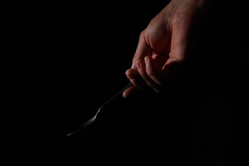 A male hand holds a small spoon from which white matter is poured out in total darkness under studio lighting