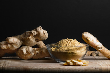 Ginger powder in glass bowl on wooden cutting board with ginger roots and slices. Healthy eating...