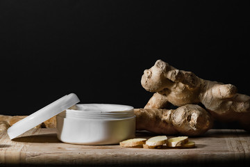 Cosmetics body cream container on wooden table. ginger roots and slices. 