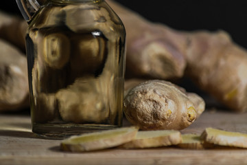 Ginger oil bottle with ginger roots and slices on wooden cutting board. Healthy eating concept. Close up, black background.