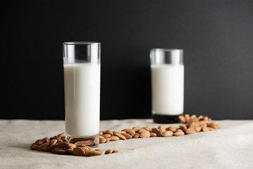 Glass of almond milk on table with almonds and unfocused glass of milk on background. Almond milk lactose free milk substitute concept. Copy space.