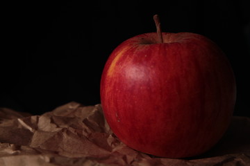 Ripe red apple on kraft paper and dark background under studio lighting