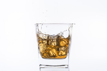 Whiskey with ice. Rum with ice. Brown brandy with ice. Three ice cubes in a glass with alcohol.  Сubes fall into a glass with splashes.