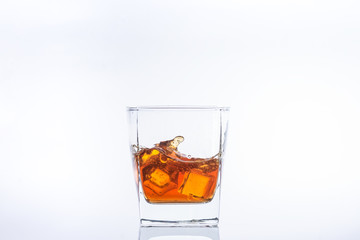 Two ice cubes in a glass of whiskey with splashes. Ice cubes in a glass with alcohol