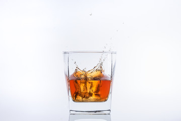 Alcohol in the glass. Whiskey and ice. Rum with ice. Brown brandy with splashes. Ice cube falls into a glass with splashes