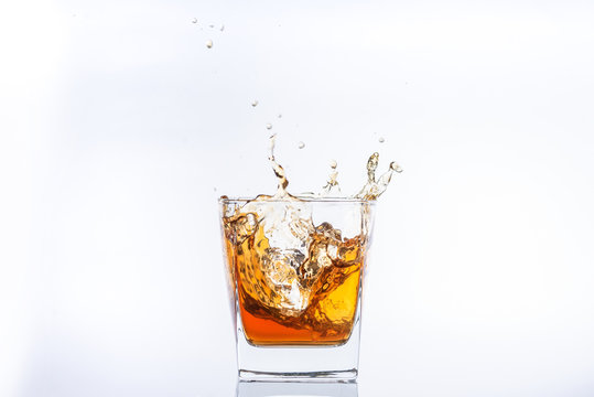 Whiskey and ice. Rum with ice. Brown brandy with splashes. Ice cube falls into a glass w