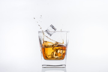 Whiskey with ice. Rum with ice. Brown brandy with ice. Ice cube falls into a glass with splashes.