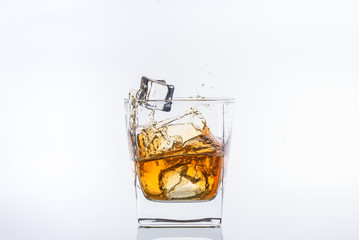 Whiskey with ice. Rum with ice. Brown brandy with ice. Two ice cubes falling with splashes into a glass with alcohol