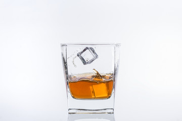 Whiskey with ice. Rum with ice. Brown brandy with ice. Two ice cubes falling with splashes into a glass with alcohol