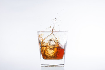 Whiskey and ice. Rum with ice. Brown brandy with splashes. Ice cube falls into a glass with splashes