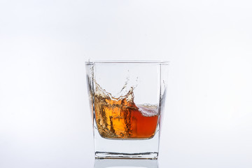 Alcohol drinks. Whiskey with ice. Rum with ice. Brown brandy with ice. Ice cube falling with splashes into a glass with alcohol