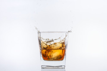 Alcohol drinks. Whiskey with ice. Rum with ice. Brown brandy with ice. Ice cube falling with splashes into a glass with alcohol