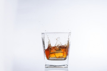 Whiskey and ice. Rum with ice. Brown brandy with splashes. Ice cube falls into a glass with splashes