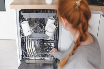 Housework: young woman putting dishes in the dishwasher