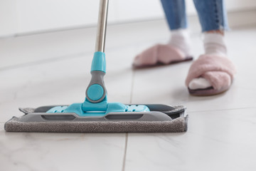 Housewife mopping floor made of porcelain tiles in the kitchen.