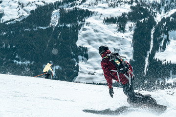Freeride snowboarder rolls on a snow-covered slope leaving behind a snow powder against the blue sky