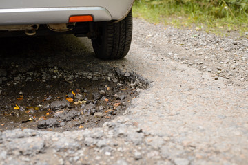 Close up picture of back of the car driving through huge deep pothole in the asphalt road