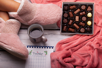 chocolate pralines and coffee by the feet of a girl in home slippers