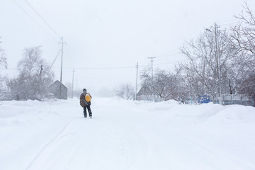 Fototapeta na wymiar A rustic man is walking down the street in winter with a yellow backpack. Snow blizzard